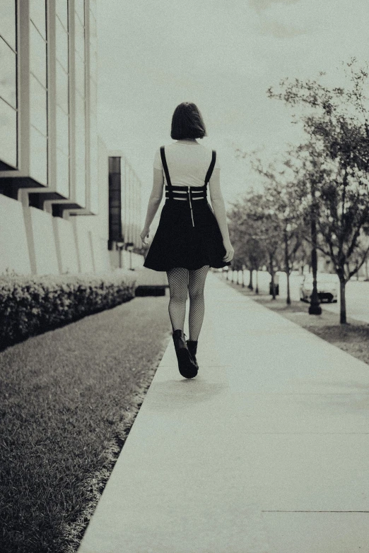 the girl walks down the sidewalk as she carries a suitcase