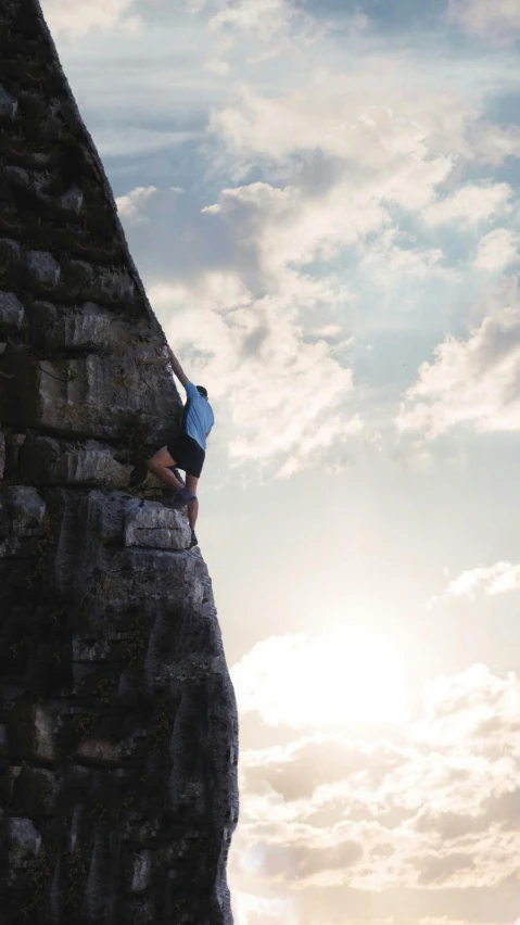 person climbing up a very tall cliff under the cloudy sky