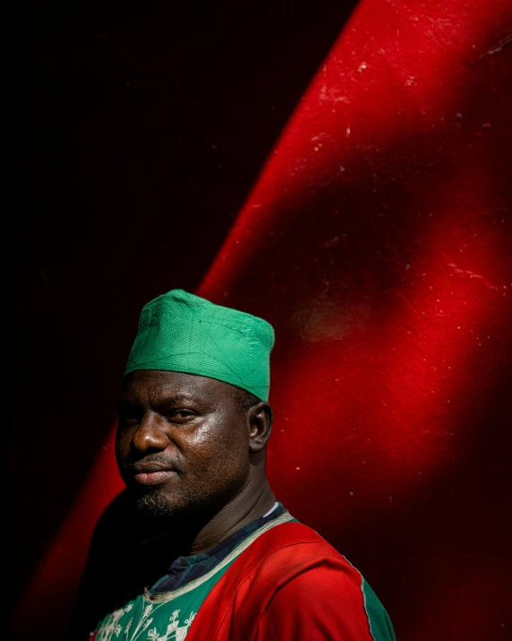 a man wearing a hat and standing in front of red fabric