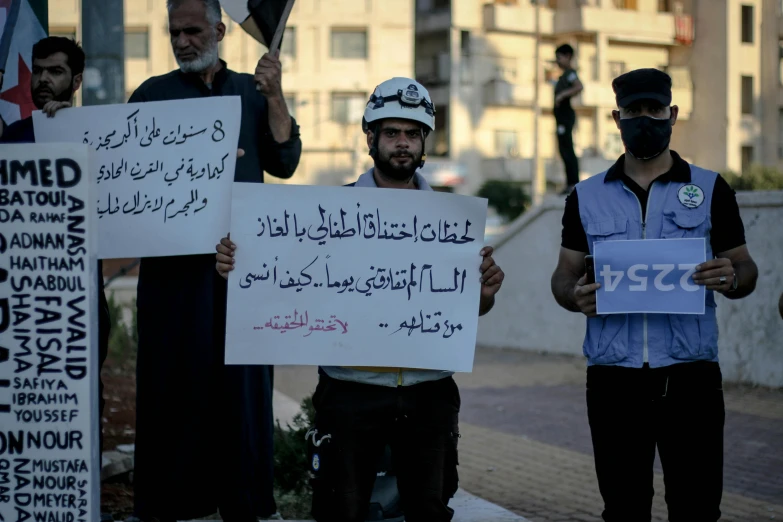 two men hold up protest signs with other protesters in the background