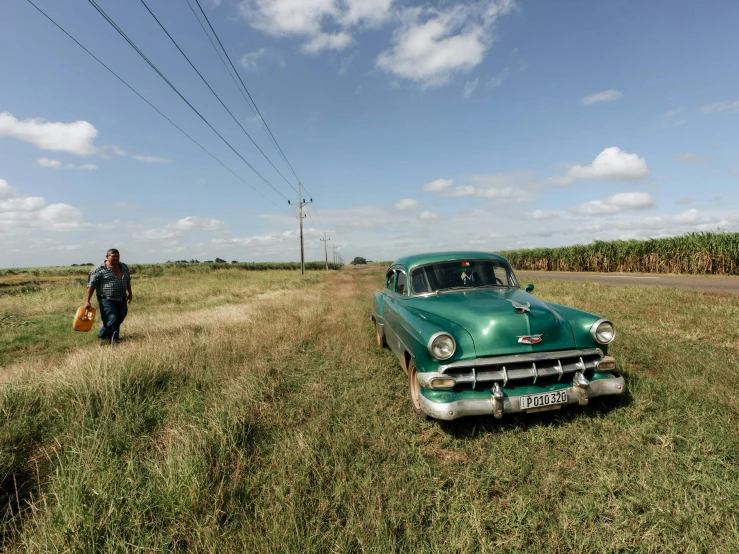 a man walks towards an old green car in the middle of a field