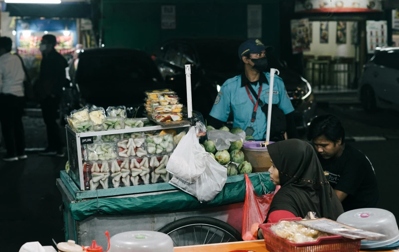 two people sitting on the ground near a fruit cart