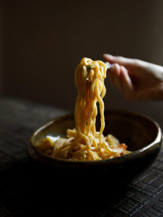 a hand holding a plate with noodles and sauce