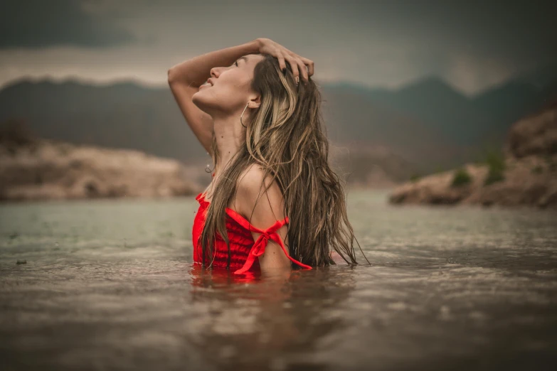 a beautiful woman sitting in the water next to a mountain