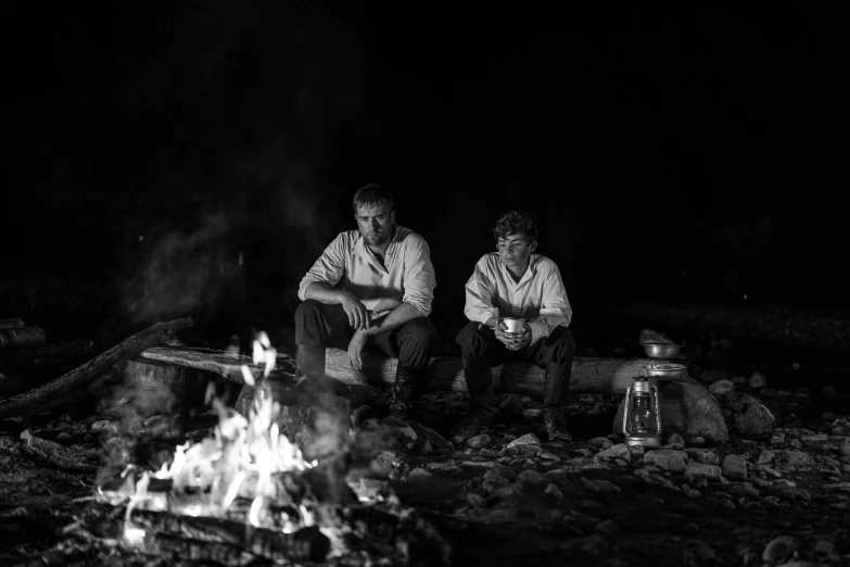 two men sitting in front of a camp fire