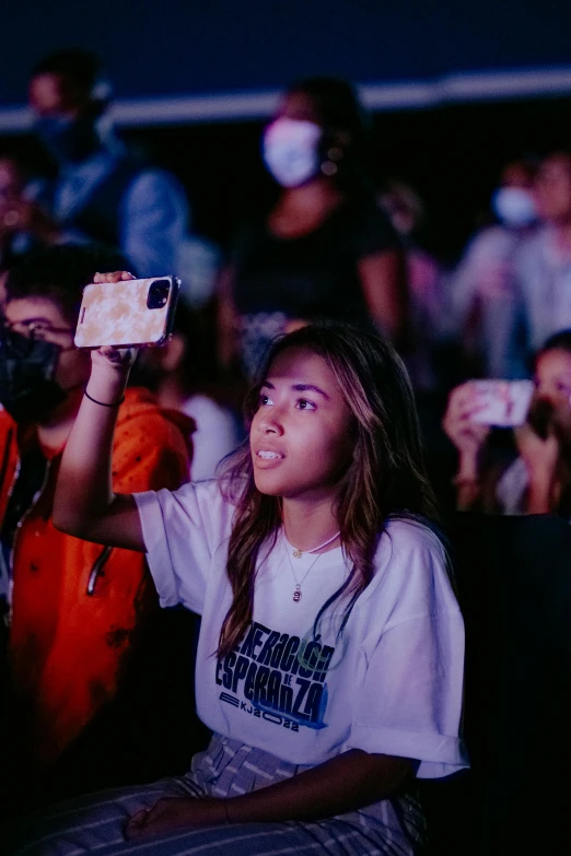 a girl holding up a smart phone at a concert