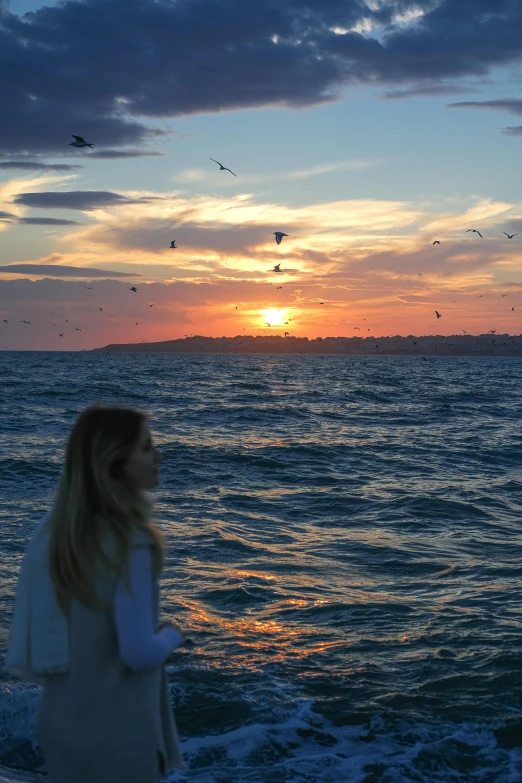 a woman walking into the water at sunset