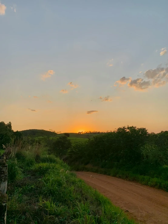 the sun rises in a clear blue sky over an unpaved road