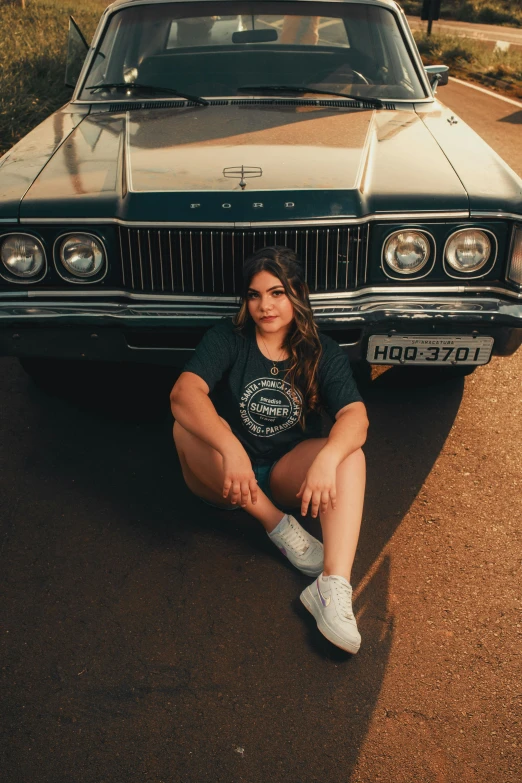 a girl is sitting on the ground beside a parked car