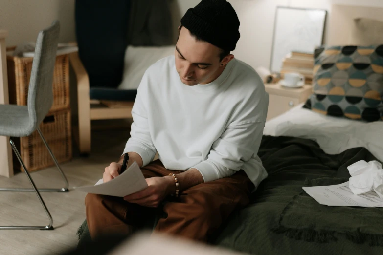 a man sitting in a bedroom writing on a piece of paper