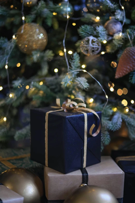 a black gift box wrapped in twine with presents underneath a christmas tree