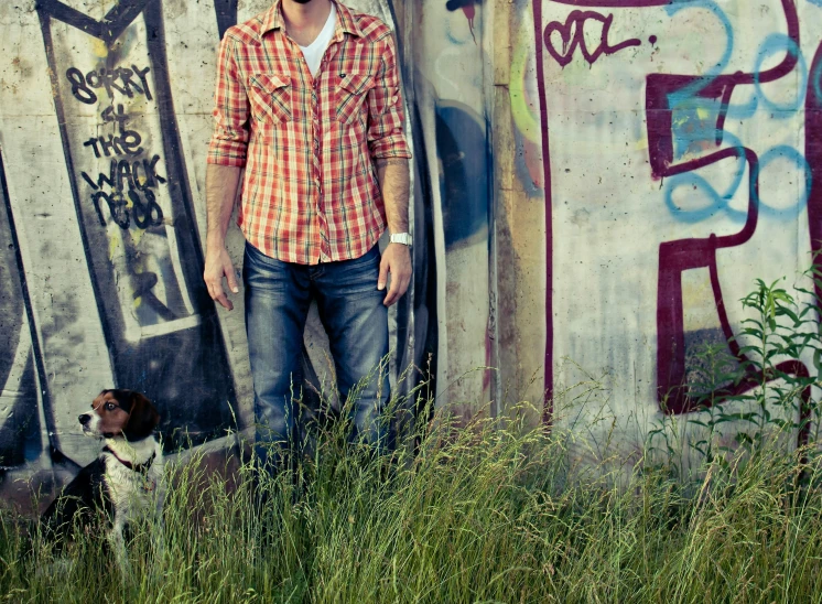 a man and dog standing in front of a wall with graffiti