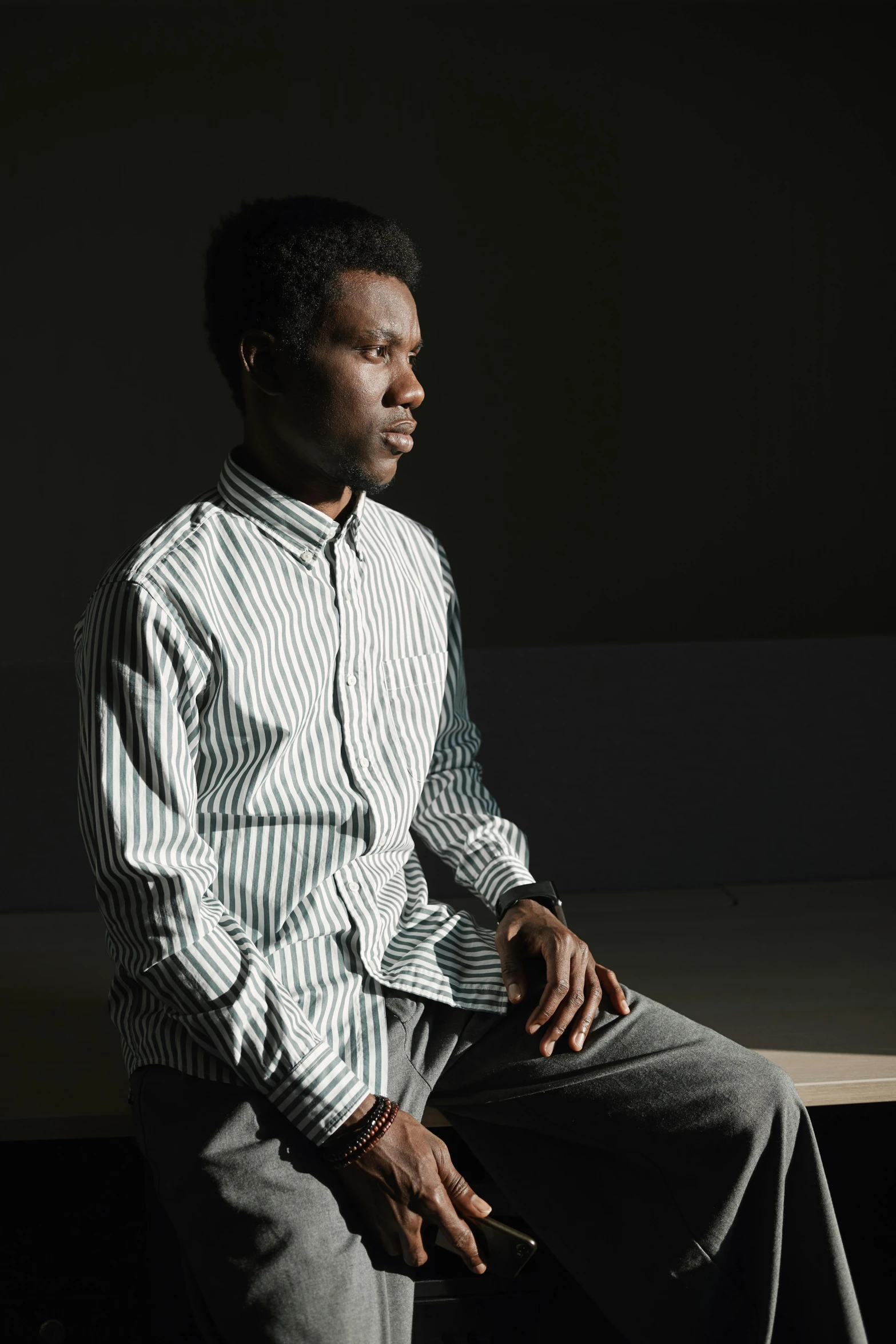 a black man in a striped shirt sitting on a wooden bench