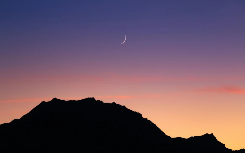 a large hill and a clear blue sky at sunset