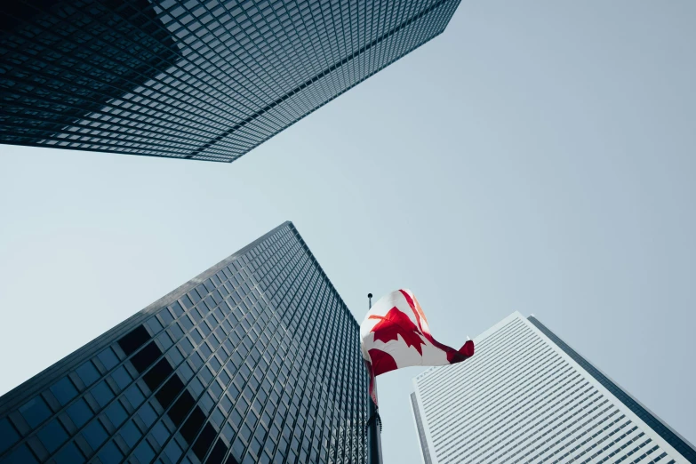 a canadian flag with a maple leaf on it flying high in the sky between tall buildings