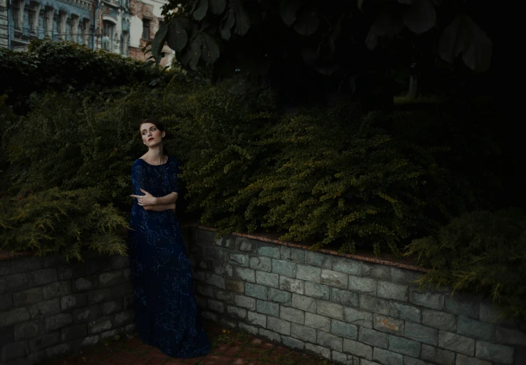 a woman in a blue dress standing in front of a brick wall