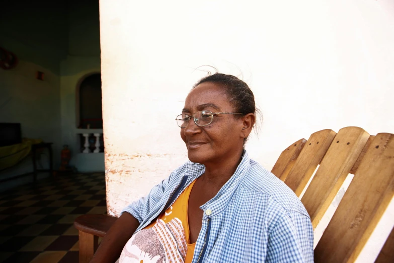 an african american woman wearing glasses sits on a wooden chair