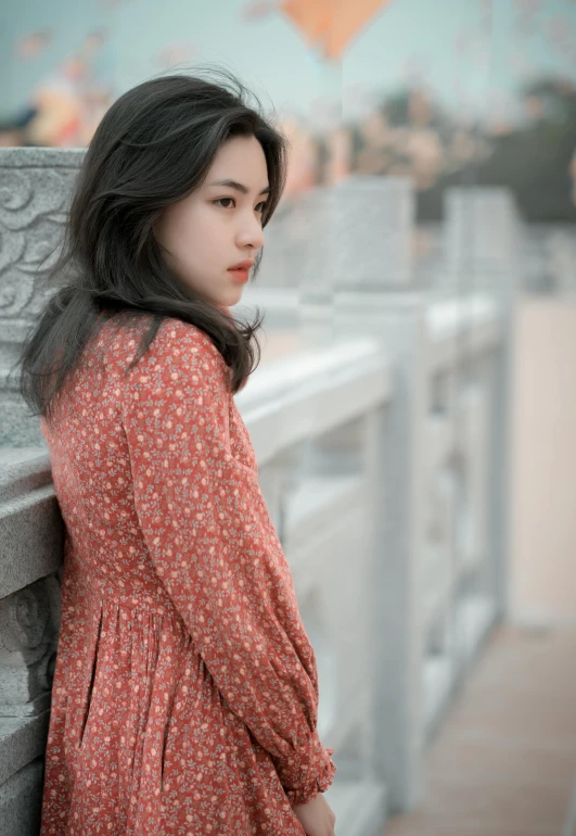 an asian woman in a dress leans against a stone wall