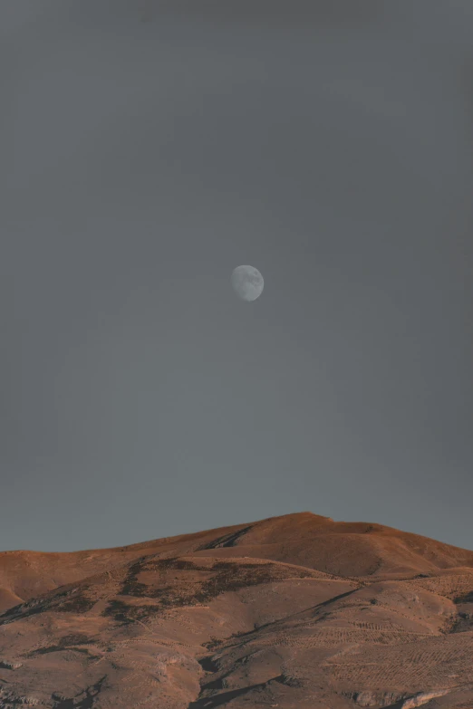 the moon is shining behind a small rocky hill