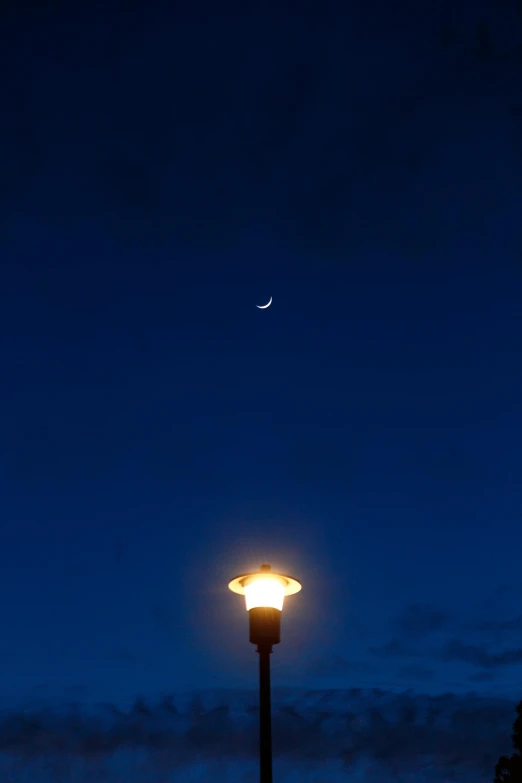 the moon shines on the dark blue sky over a light post