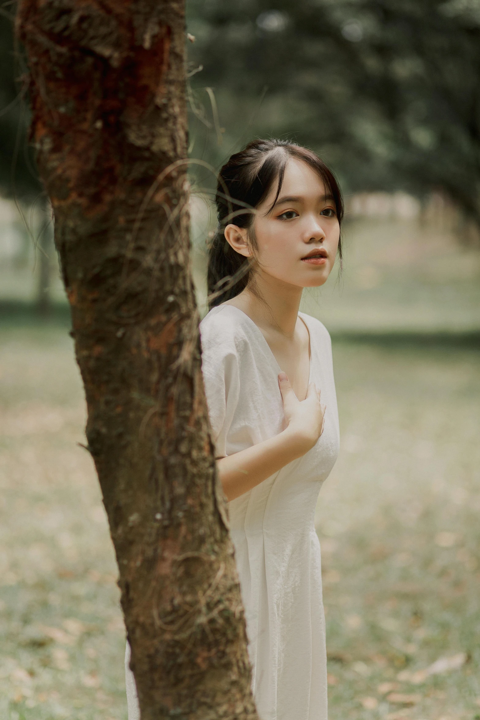 a woman standing in front of a tree wearing white clothing