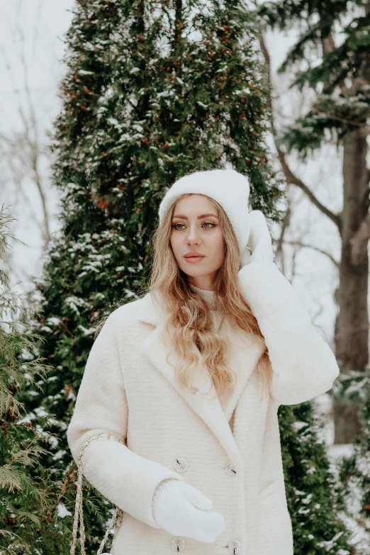 a blonde woman wearing a white coat and hat in a snowy area