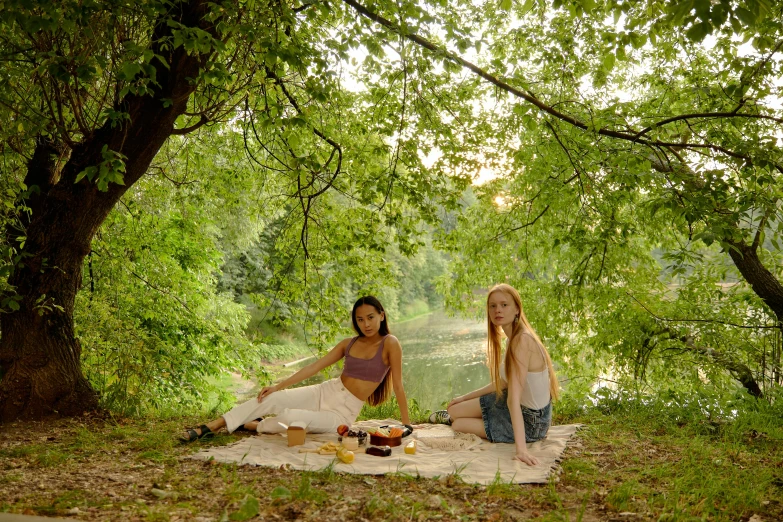 two woman sitting on a blanket eating dinner and posing for the camera