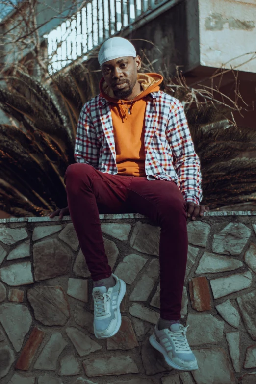a man with his legs crossed wearing an orange and white checked shirt, red pants and blue and black tennis shoes