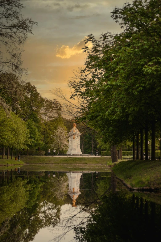 the reflection of a statue of a woman standing next to a body of water at sunset