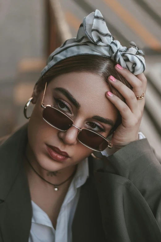 a woman in sunglasses and a head scarf has her hands on her forehead