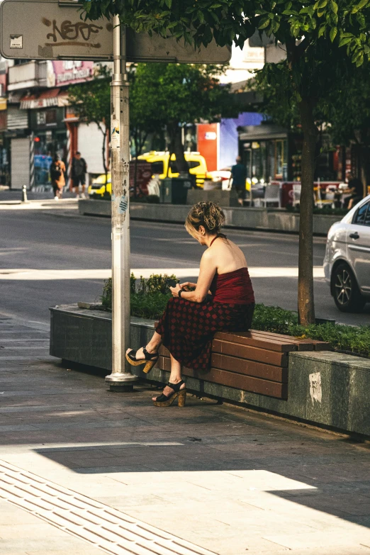 a woman wearing sandals sitting on a bench next to a city street