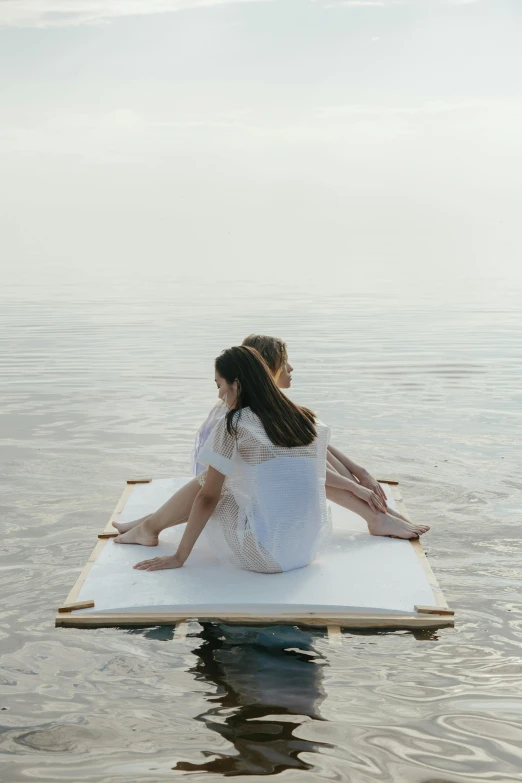 two woman sitting on a floating platform and one standing up