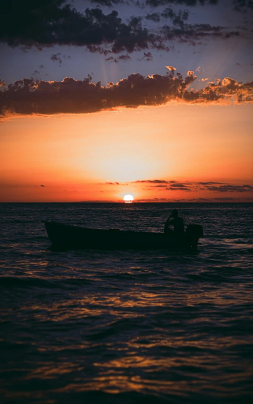 the setting sun shines brightly in the ocean with two people in a small boat on the water