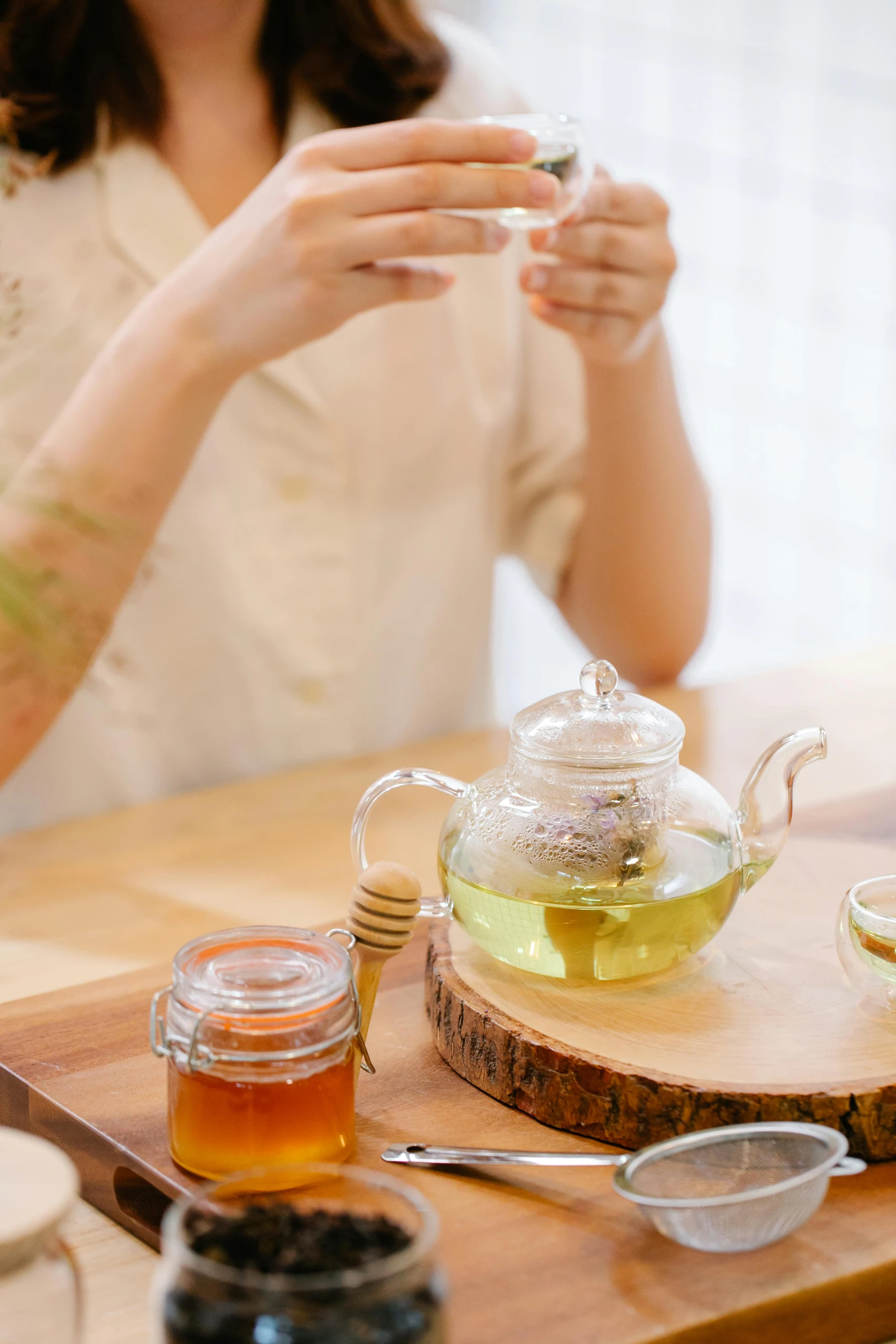 a woman holding a small glass teapot over a tea set