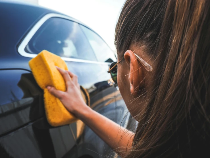 a woman cleans the side of her car