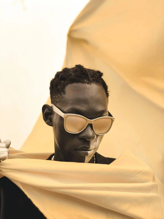 a man with sunglasses covering himself behind a yellow sheet