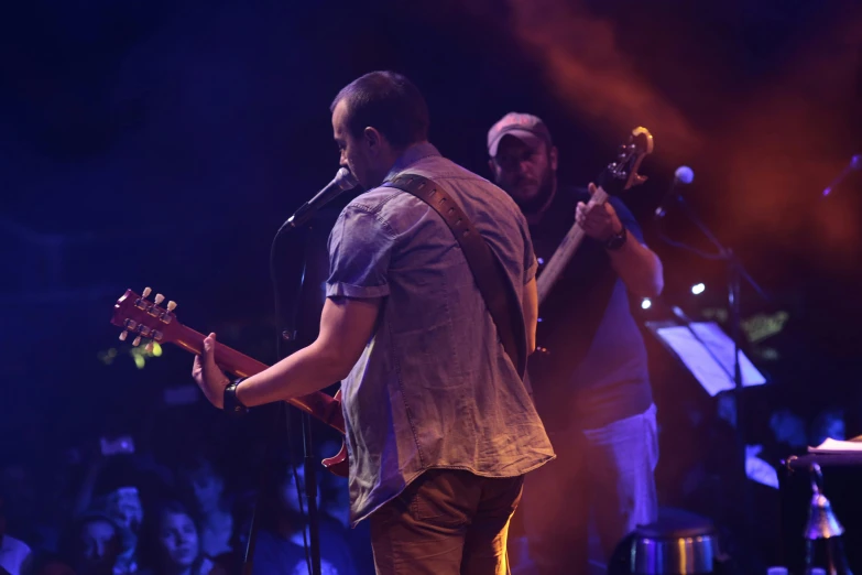 two men sing and play guitar on a stage