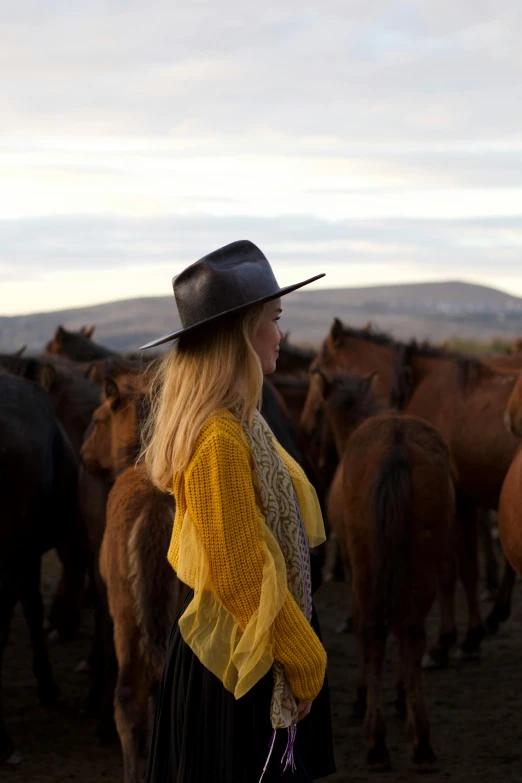 a  wearing a black hat while standing next to horses