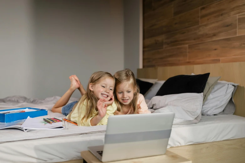 two girls sitting on a bed using a laptop computer