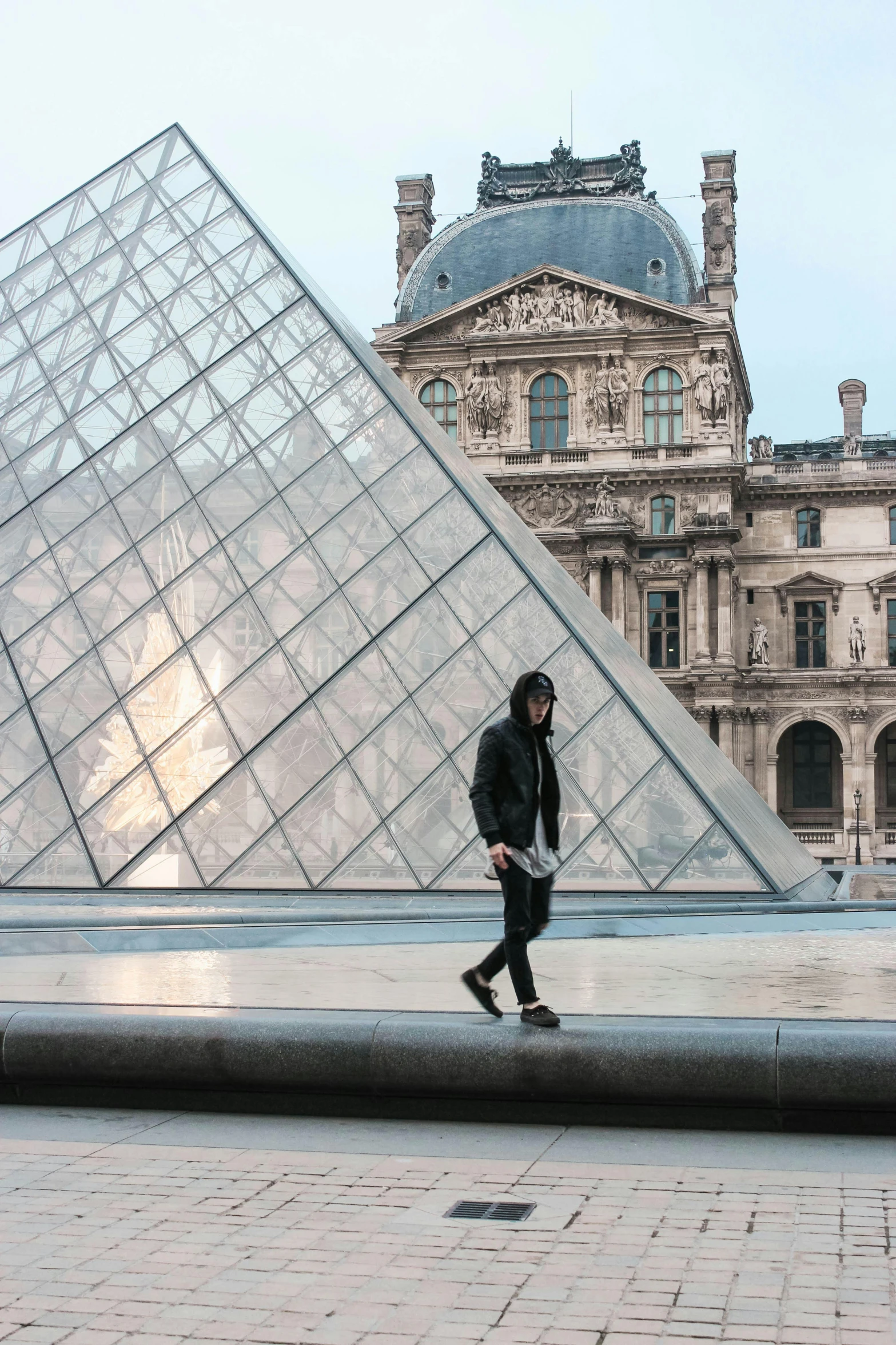 a woman walking next to a building with a huge glass triangle in the background