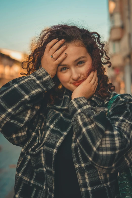 a woman wearing a plaid coat holding her hand up to her face