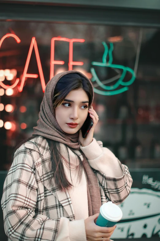 a girl with a scarf and a coffee cup talking on the phone