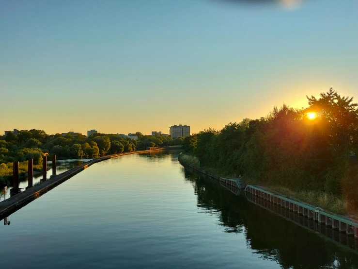 the sun sets over a river that is surrounded by trees