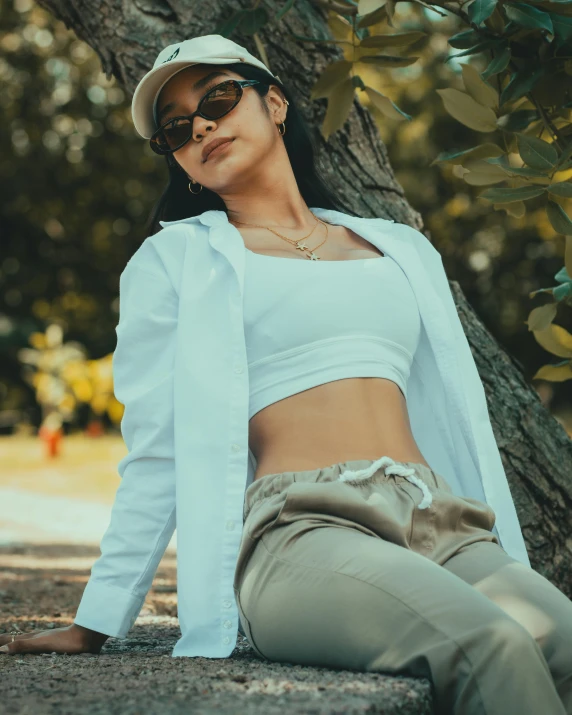 a woman wearing sunglasses and a baseball cap leaning against a tree