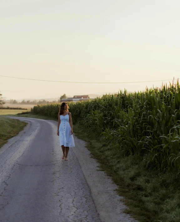 a woman is walking down a dirt road near a field
