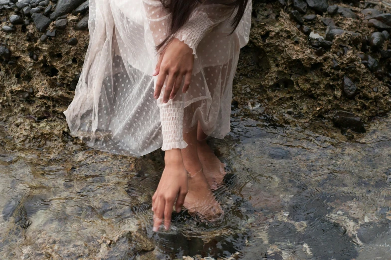 a girl sitting in shallow water with her bare foot touching her hands