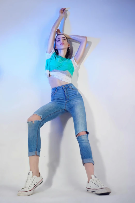 a woman wearing ripped jeans, blue top, and white converse shoes is stretching her arms up