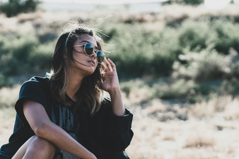 a girl wearing sunglasses is sitting in the dirt and looking into the distance