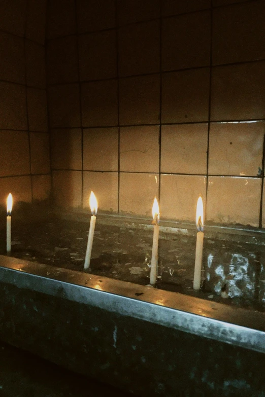 three candles burning in a stone shrine with an unlit mirror behind them