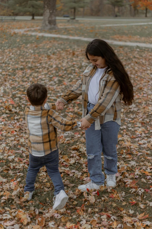 a little boy standing next to a little girl in front of leaves